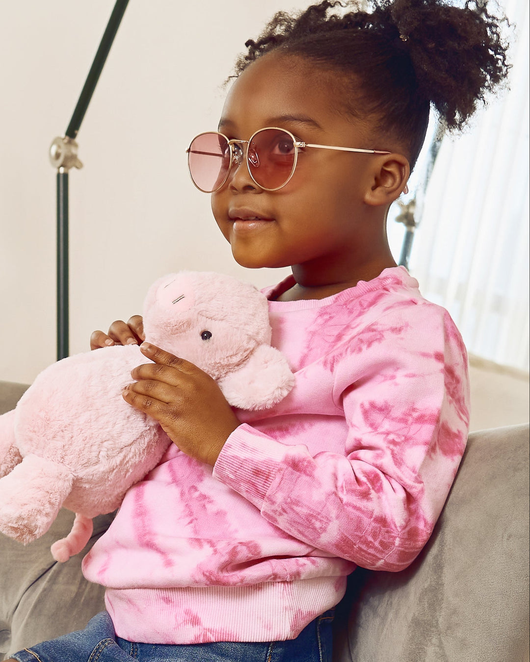 Child wearing a pink tie-dye sweatshirt and sunglasses, holding a pink teddy bear.