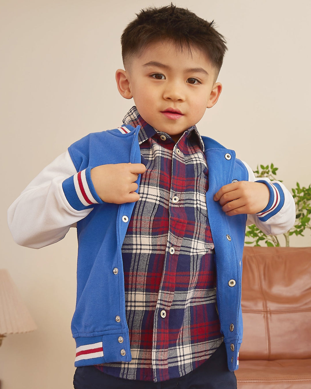 Child wearing a blue vest over a plaid shirt in a living room setting